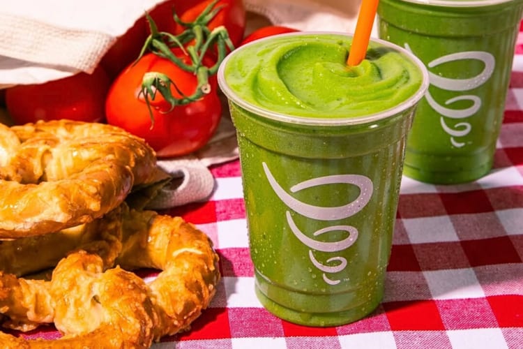 Two Jamba Juice green smoothies next to tomatoes and pretzels