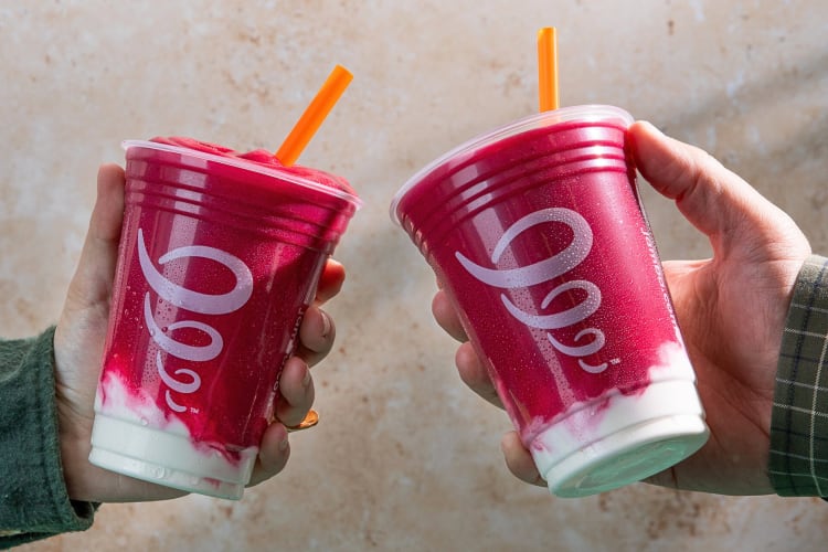 Two hands holding two purple and white Jamba Juice smoothies
