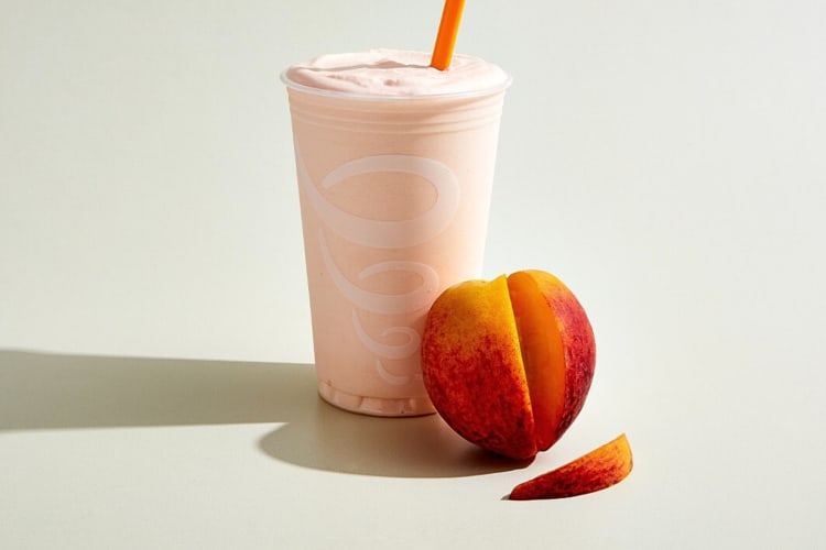 A peach-flavored Jamba Juice smoothie next to a peach