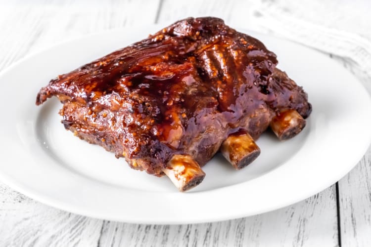 Pork spare ribs served with barbecue sauce on a ceramic plate