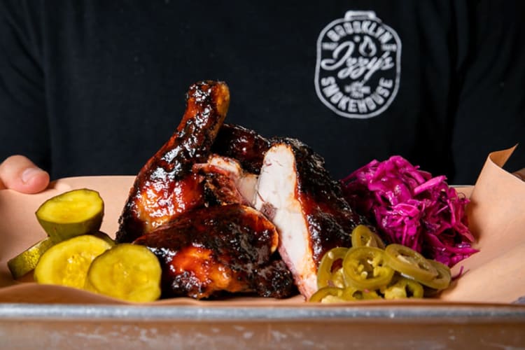 A person holding a tray with barbecue meat, pickles and slaw