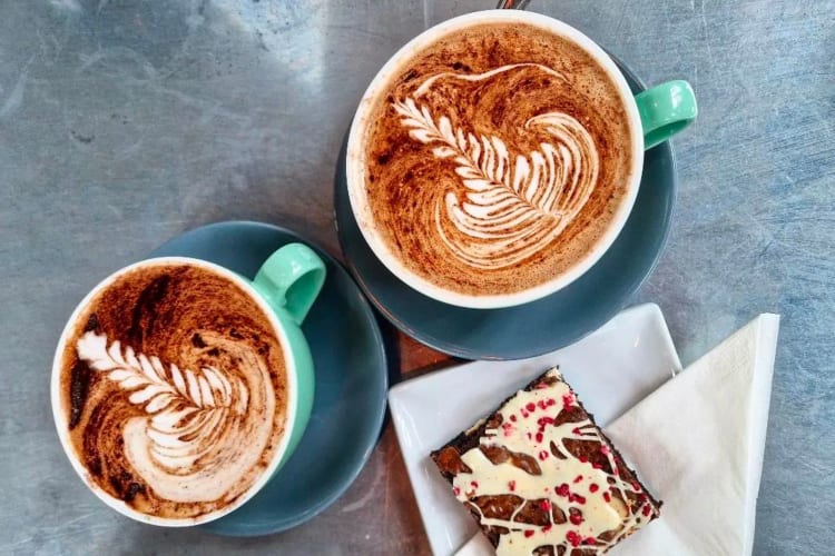 Two coffees with latte art with a chocolate brownie. 