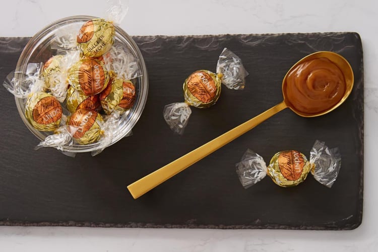 Lindor Dulce de Leche truffles and a spoonful of chocolate on a black board