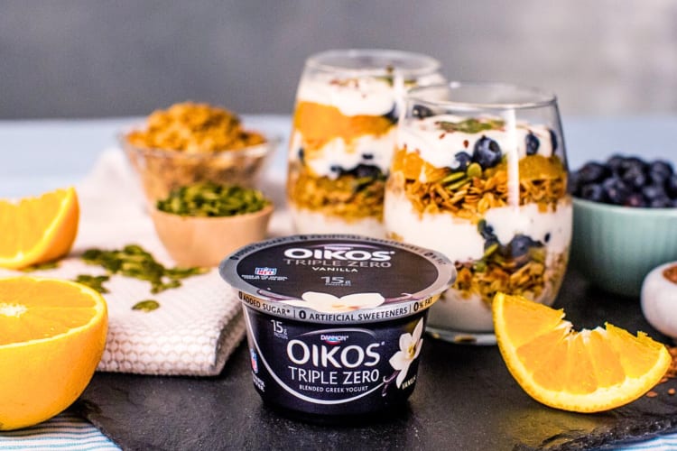 A Oikos Triple Zero low-calorie yogurt in front of two desserts in clear glasses and fruit