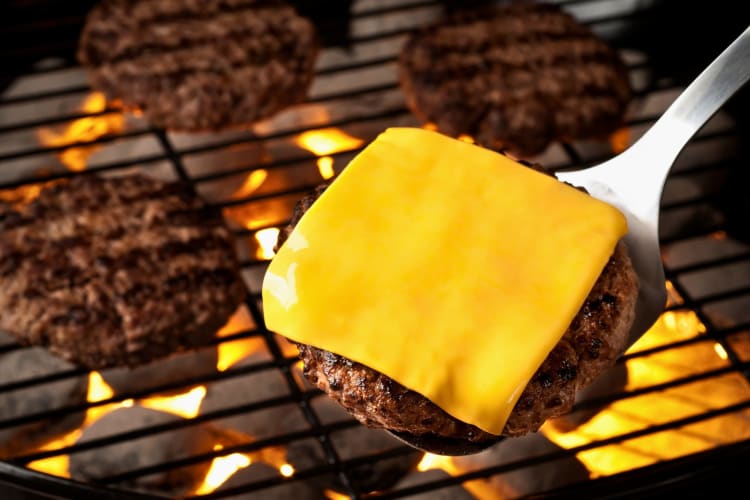 A beef patty topped with melted cheese on a spatula
