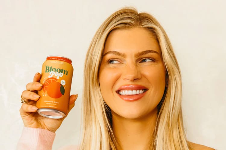 A woman smiling and holding up a prebiotic soda.