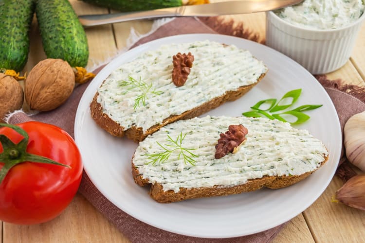 Two slices of bread topped with cheese spread, next to vegetables