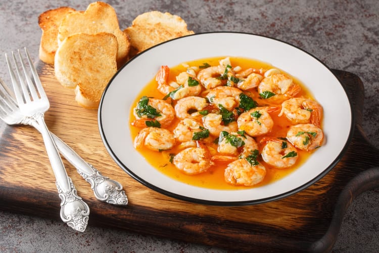 Gambas al pil pil, a tasty Malaga food, next to two forks and toast slices