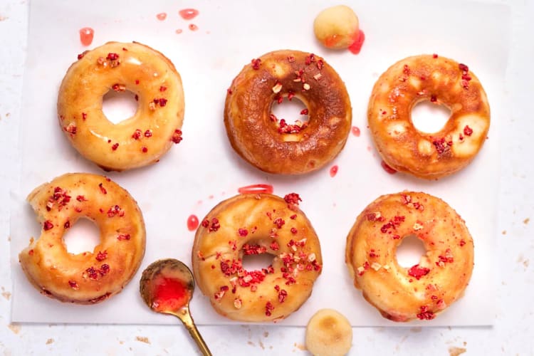 Aerial view of six strawberry doughnuts and a gold spoon