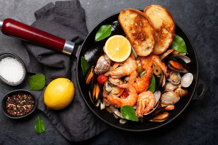 A variety of seafood and two pieces of toasted bread in a pan