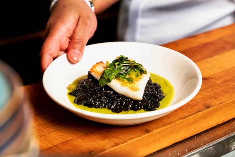 squid ink rice dish topped with fluk