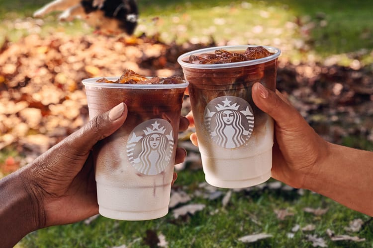 Two hands clinking Starbucks coffees in clear takeaway cups