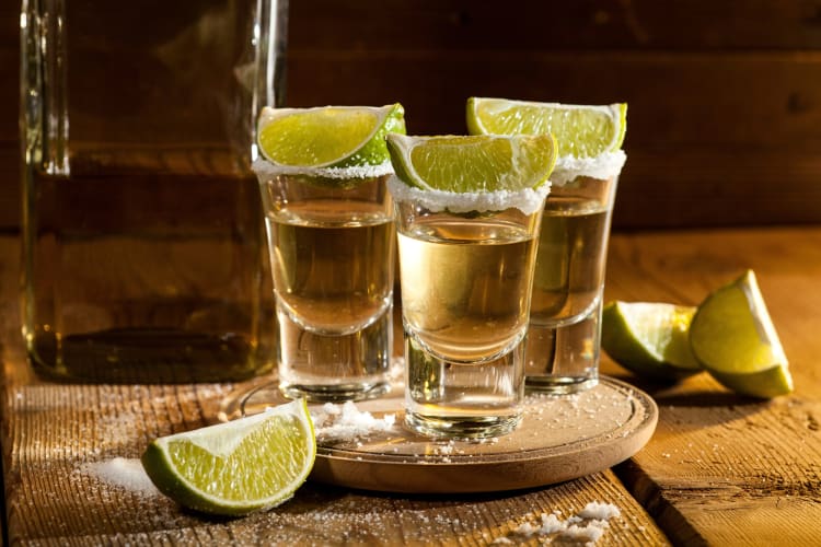 Three shots of tequila with lime wedges and salt