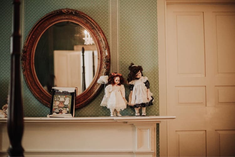 two spooky-looking old dolls in front of a mirror in an old house