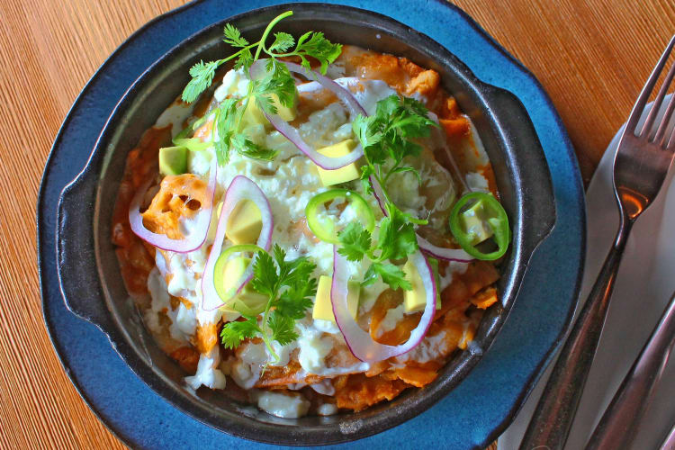 Chilaquiles served with cheese, avocado and jalapeños on a wooden table