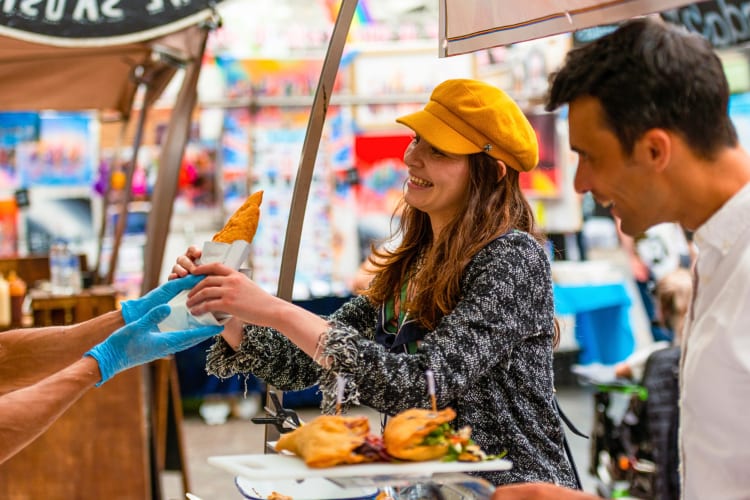 A woman grabbing a food item from a vendor during a food tour