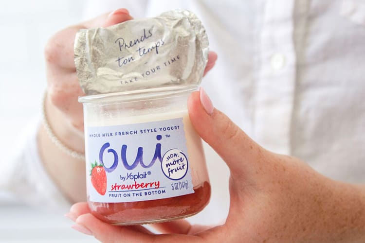 A hand peeling back the foil from a strawberry Oui yogurt flavor