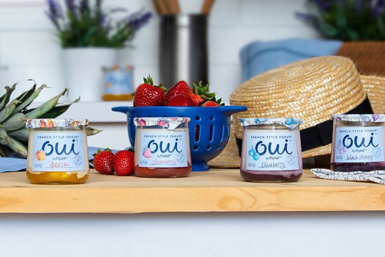 Four Oui yogurt flavors on a wooden counter in front of strawberries and a hat