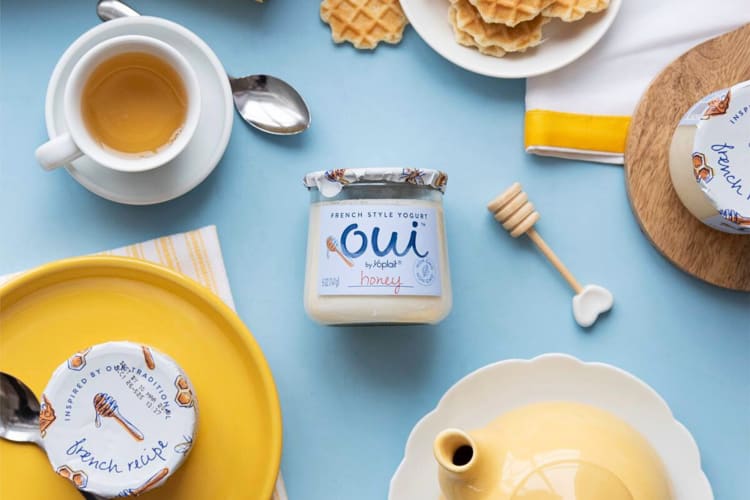 The honey Oui yogurt flavor surrounded by a cup of tea, wafers and kitchen utensils