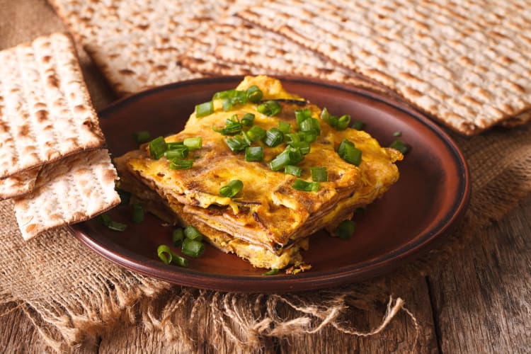 A serving of matzo brei on a brown plate, surrounded by pieces of matzo