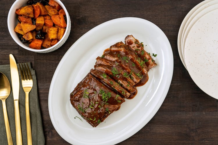 Aerial view of a brisket topped with gravy, next to vegetables