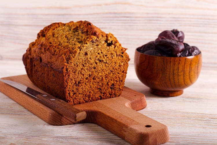 Half of a date loaf on a wooden board, next to a bowl of dates