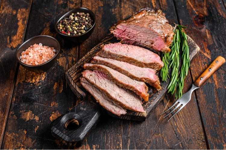 Sliced tri tip Steak on a wooden cutting board sided with salt and pepper