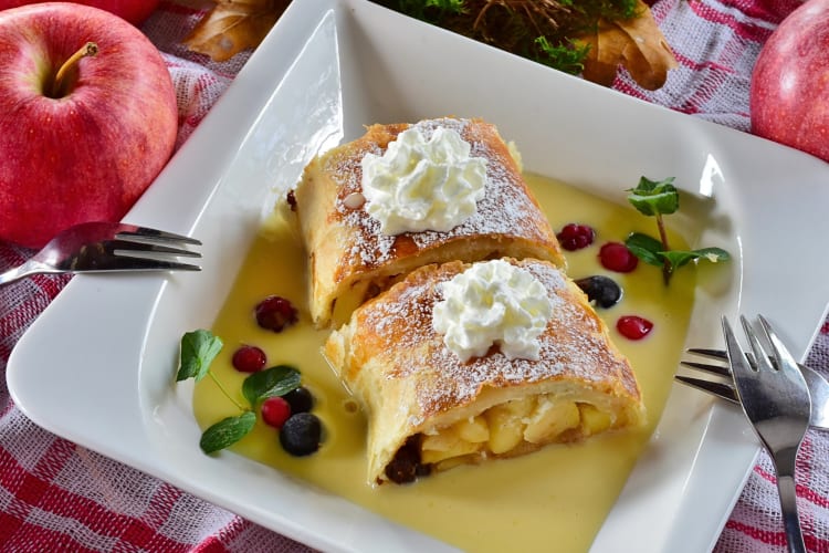 Two portions of apple strúdl topped with cream and laying in a bed of custard