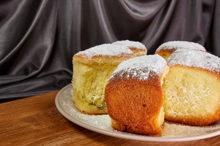 Five portions of buchty on a plate, in front of a black curtain background