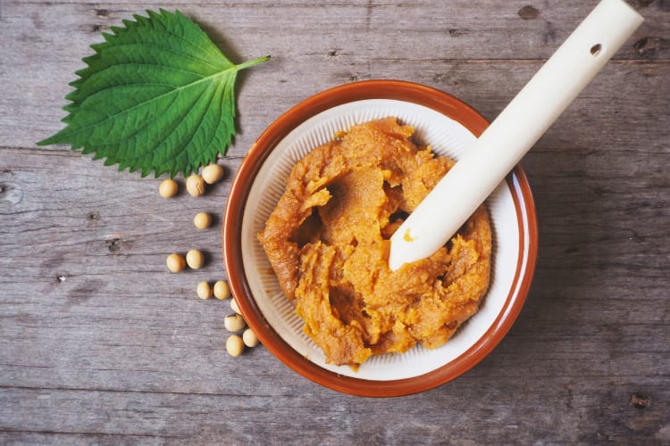 A pot of miso paste with an oba leaf and soybeans on the side.