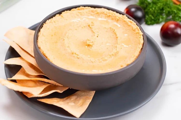 A bowl of spicy hummus served with taco chips to be dipped in it