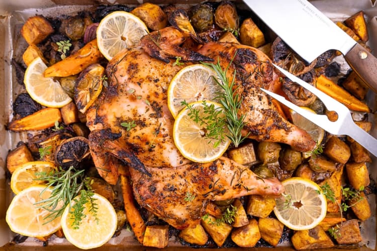Spatchcock chicken surrounded by potatoes, vegetables, lemon slices and herbs