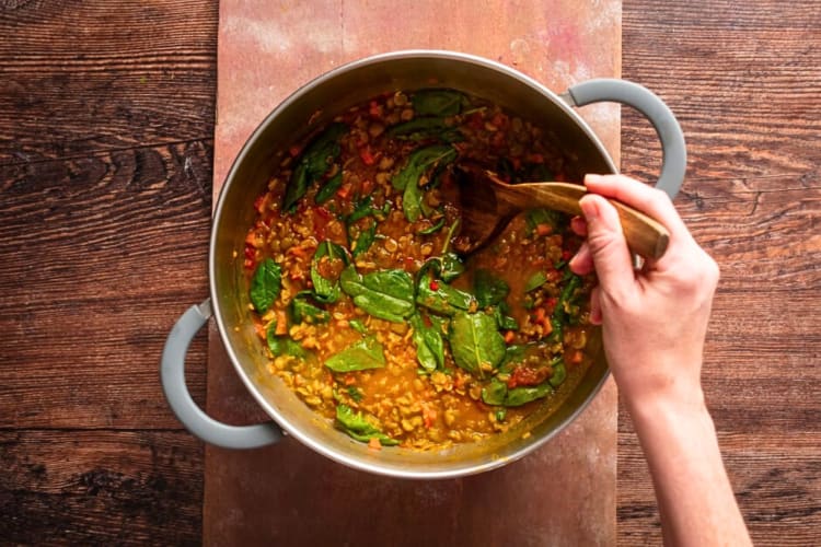 Aerial view of a hand stirring a vegan lentil soup, a popular Purim food