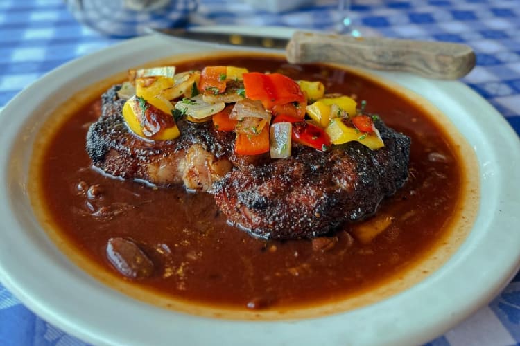 A steak in sauce topped with vegetables.