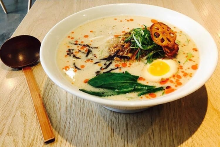 A bowl of ramen on a wooden table next to a wooden spoon