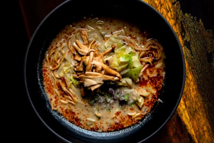 A bowl of creamy ramen on a dark wood table