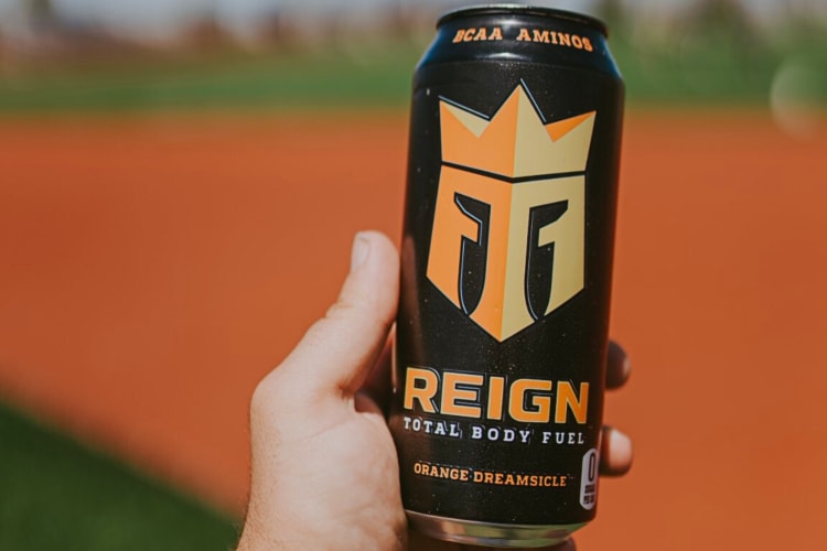 A hand holding the Orange Dreamsicle Reign energy drink flavor