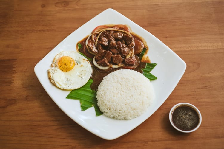 Beef lok lak on a white plate atop a wooden surface
