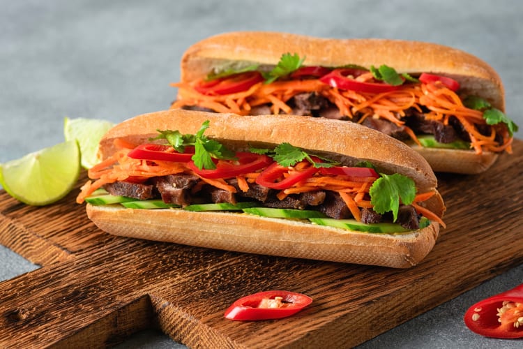 Two báhn sandwiches filled with meat and vegetables, on a wooden serving board
