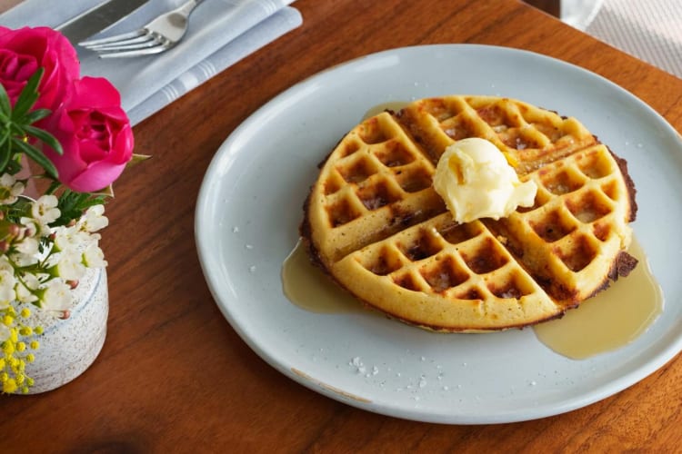 A waffle with syrup on a plate next to a flower vase