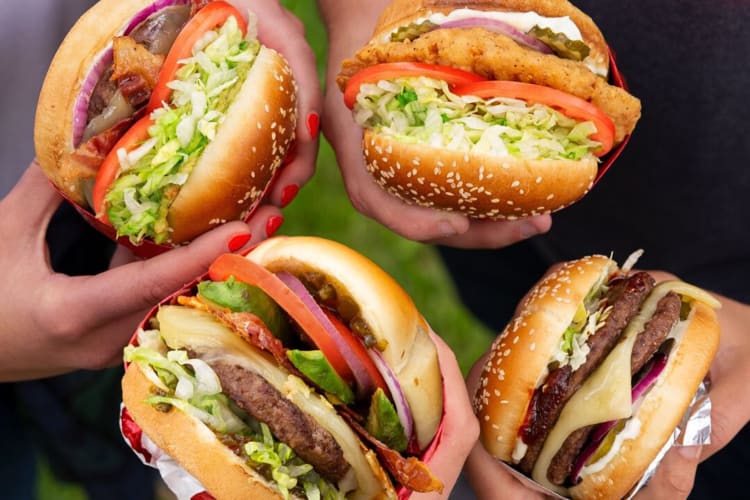 Four hands holding four burgers from Red Robin