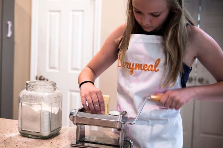 A young girl rolling pasta with a machine during a cooking class