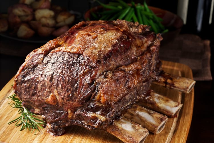 A cooked prime rib on a wooden board, with a stem of rosemary.