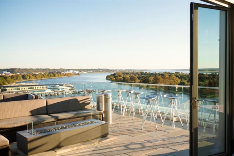 A rooftop deck with couches and other seating overlooking a river and green trees