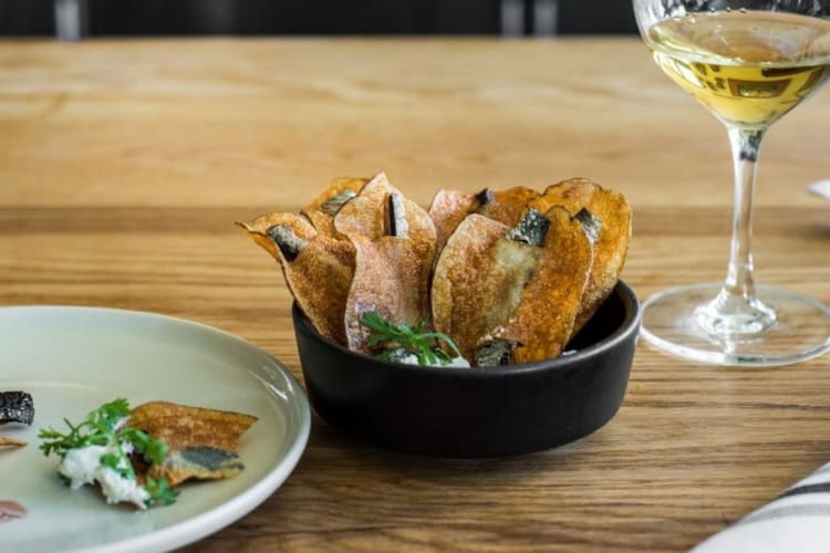 Sardines nestled in thin potato slices with a glass of wine