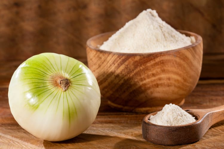 A fresh onion next to a wooden bowl of onion powder