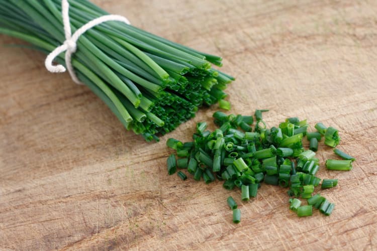 A tied bundle of chives next to chopped chives