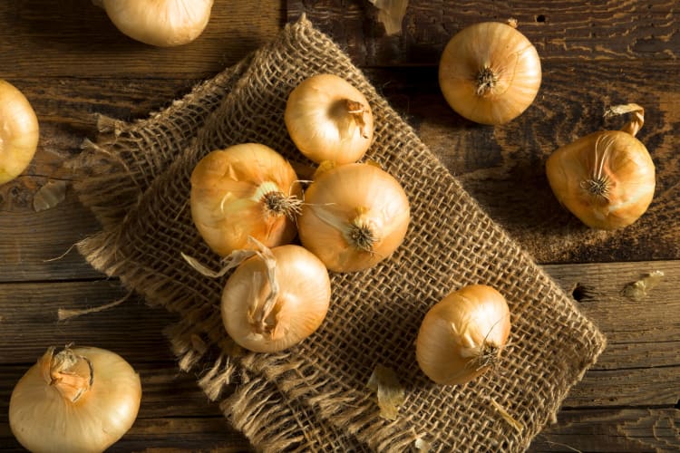 Small yellow-skinned onions on a burlap sack on a wooden surface