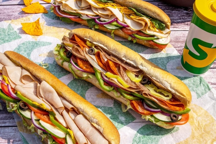 Three subways silled with ham, pepperoni, cheese and veggies