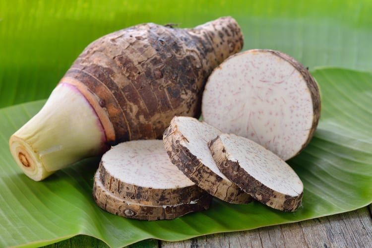 A whole taro root and taro slices on a green leaf